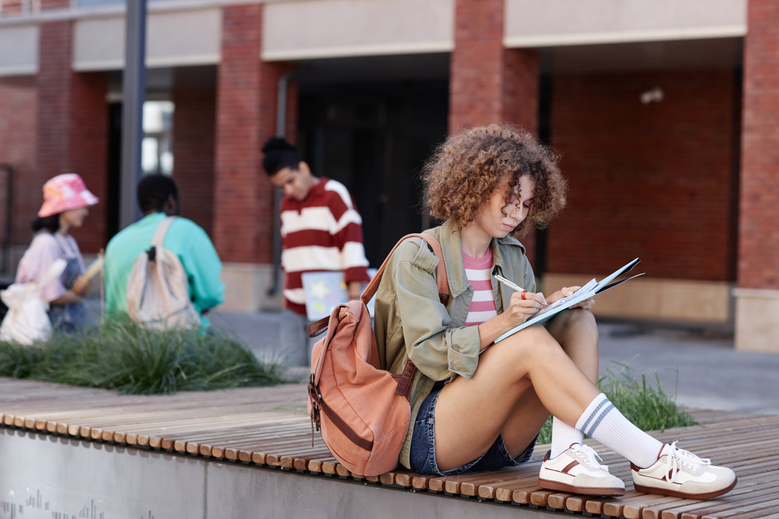 Female student sitting outdoors on college campus and writing in notebook