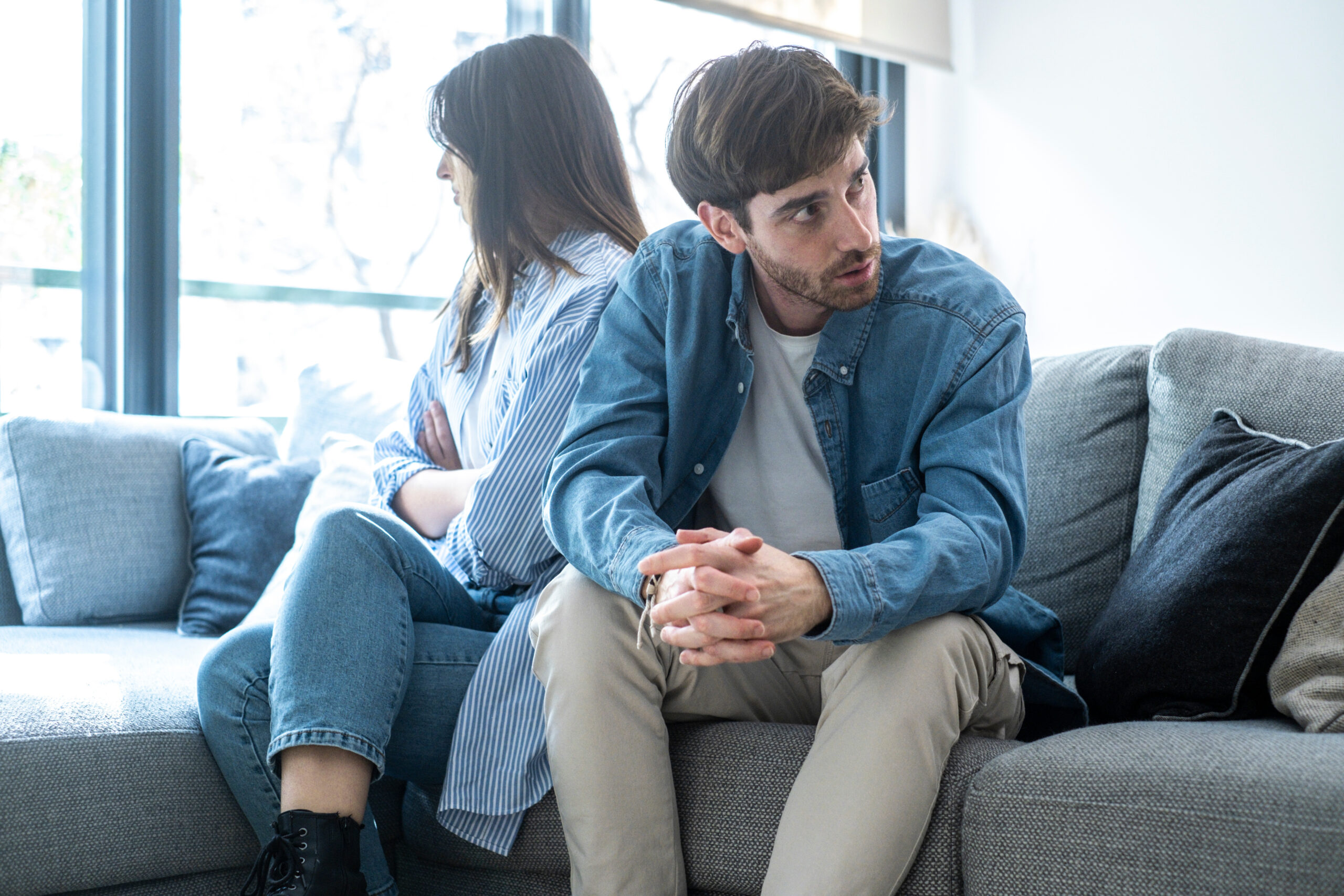 Upset couple sitting separately in their living room, ignoring each other, dealing with trust issues, marital frustration, emotional pain, cheating suspicion, and the possibility of a breakup