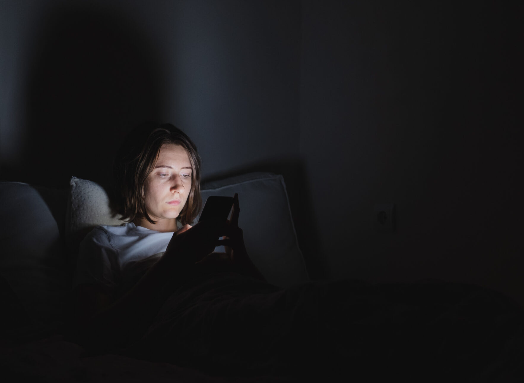 Woman in bed uses phone late at night. Insomnia or excessive usage of social media concept.