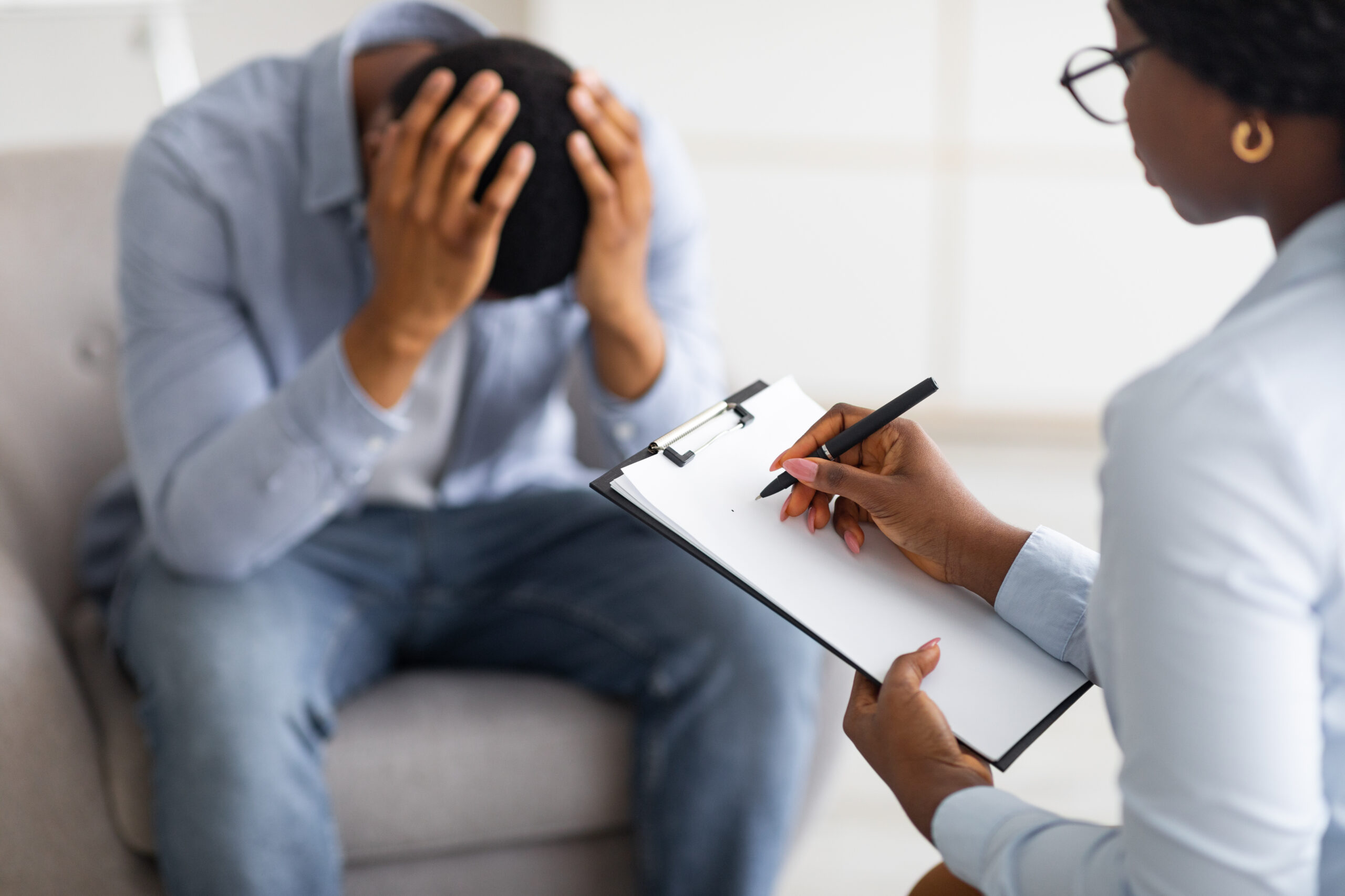 Depressed black guy holding his head at counselor's office, seeking professional help with mental disorder