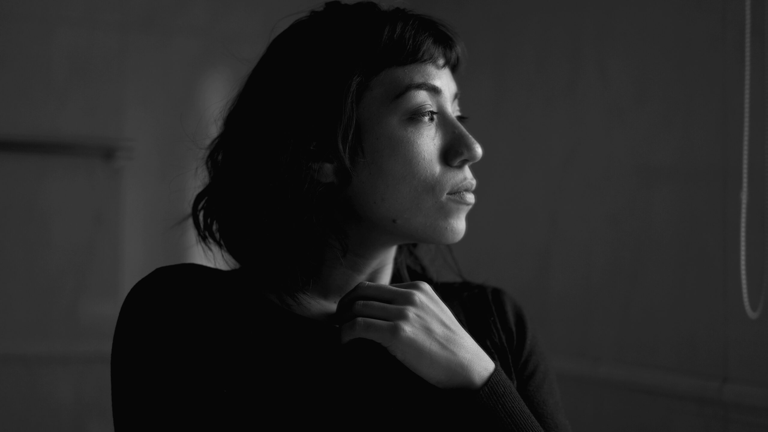 A contemplative young hispanic woman standing by window thinking. A pensive latin girl in monochromatic