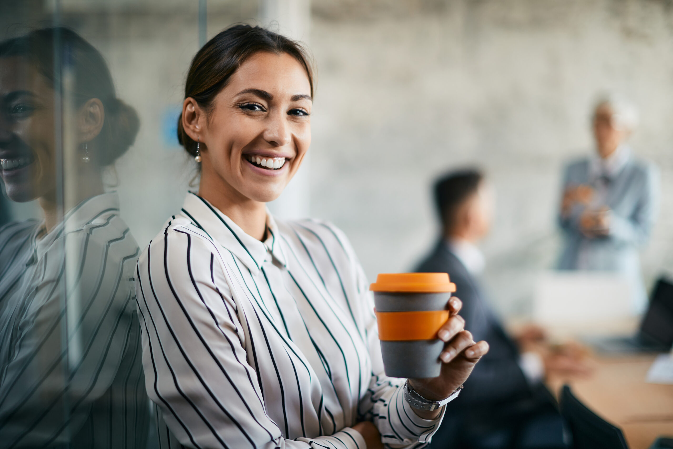 Young happy businesswoman enjoys during coffee break in the office and looks at camera.